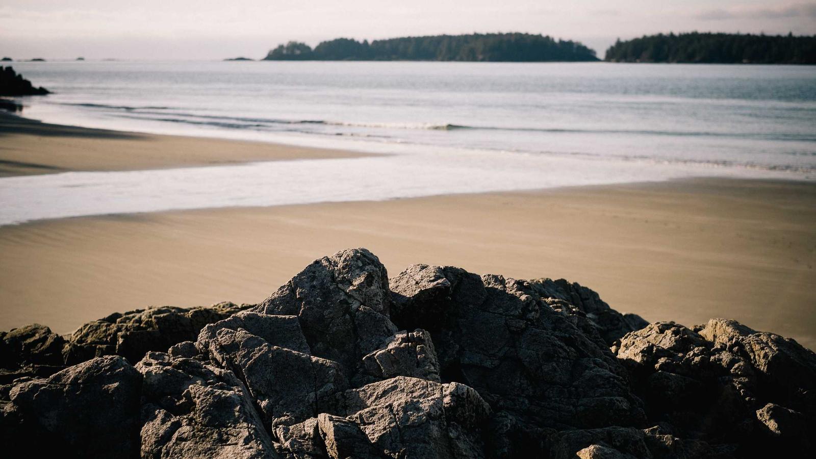 Morning light on a rocky outcrop and sandy beach with forested islands beyond (stock photo)