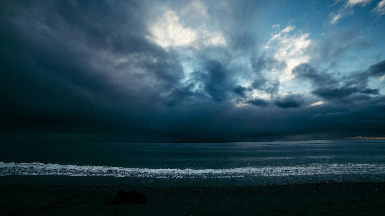 Storm clouds breaking over a dark sea at dusk (stock photo)
